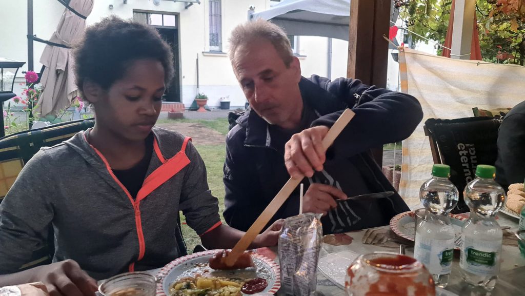 Grillveranstaltung im Garten des Kinderheim Elisabeth Stift. Kinder und Schwestern des Heims essen gemeinsam mit Mitgliedern des Vereins am Tisch in einer Gartenlaube.