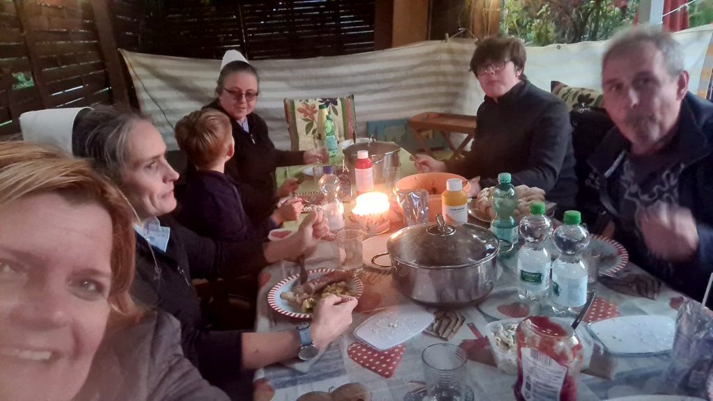 Grillveranstaltung im Garten des Kinderheim Elisabeth Stift. Kinder und Schwestern des Heims essen gemeinsam mit Mitgliedern des Vereins am Tisch in einer Gartenlaube.