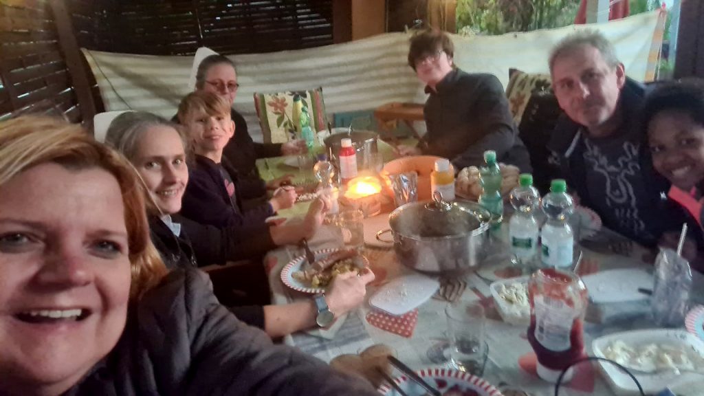 Grillveranstaltung im Garten des Kinderheim Elisabeth Stift. Kinder und Schwestern des Heims essen gemeinsam mit Mitgliedern des Vereins am Tisch in einer Gartenlaube.